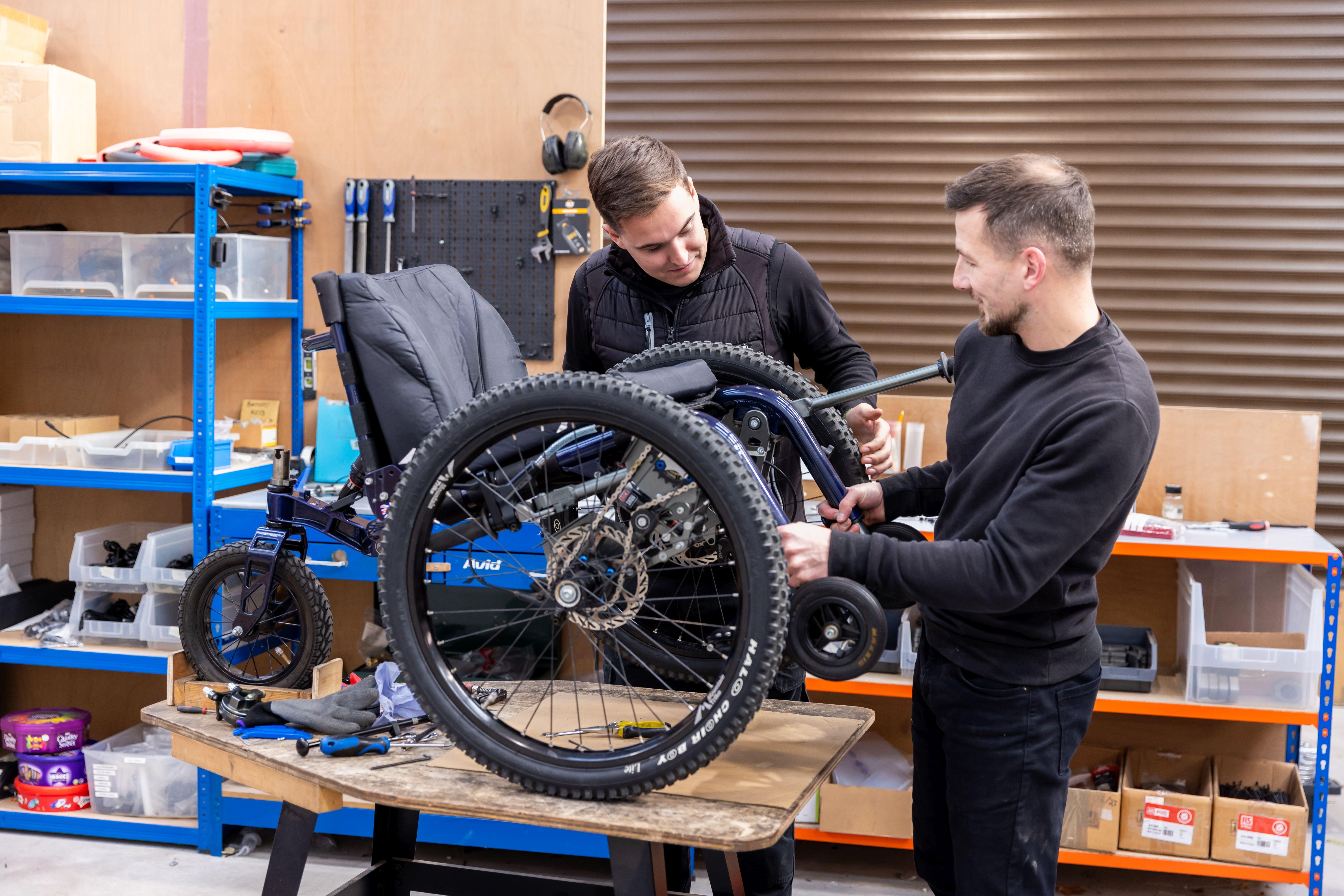 Mountain Trike wheelchair on a workshop bench being serviced by two men