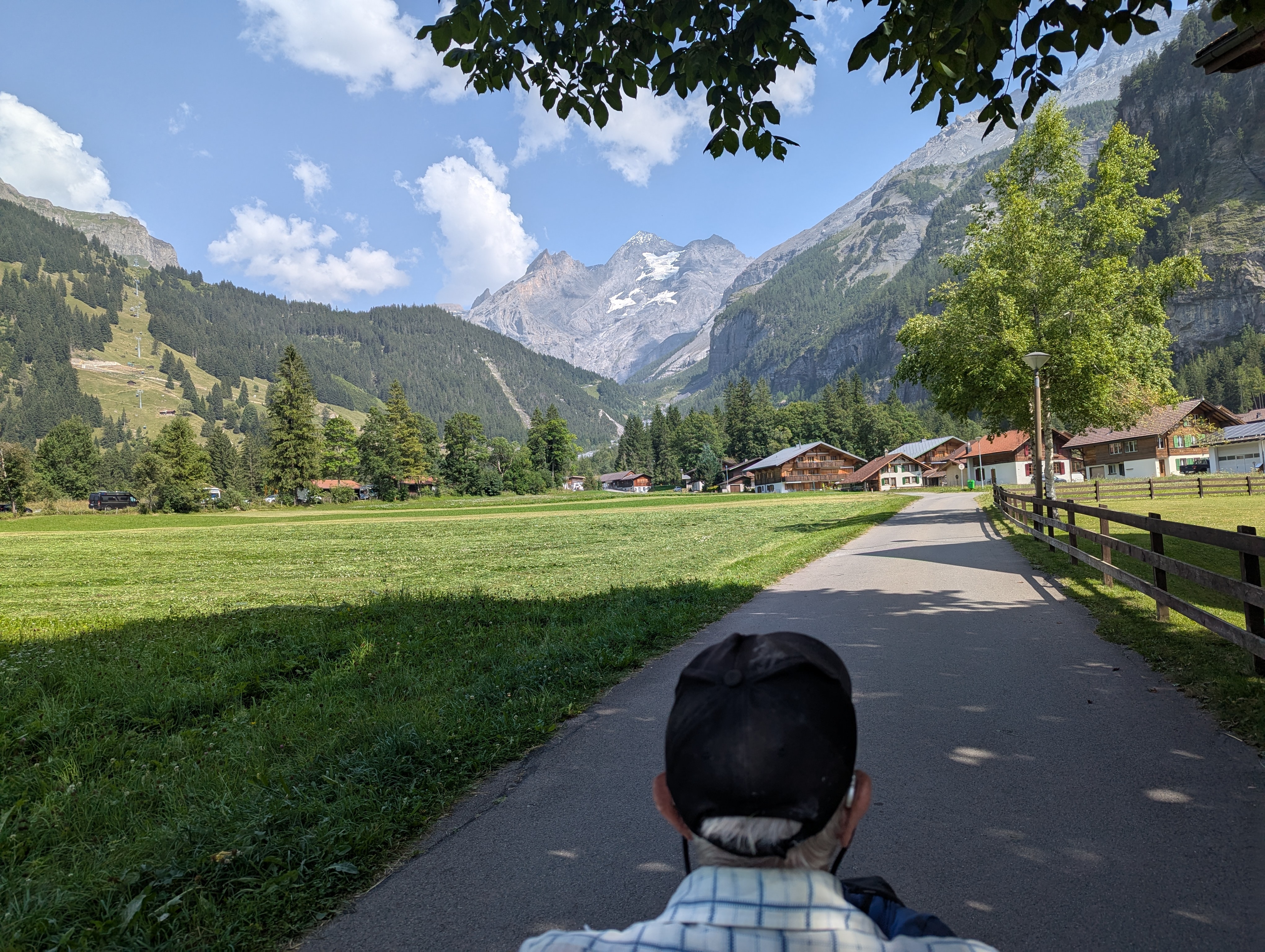 man in an all terrain wheelchair on a path taking in the mountain views and mountain chalets