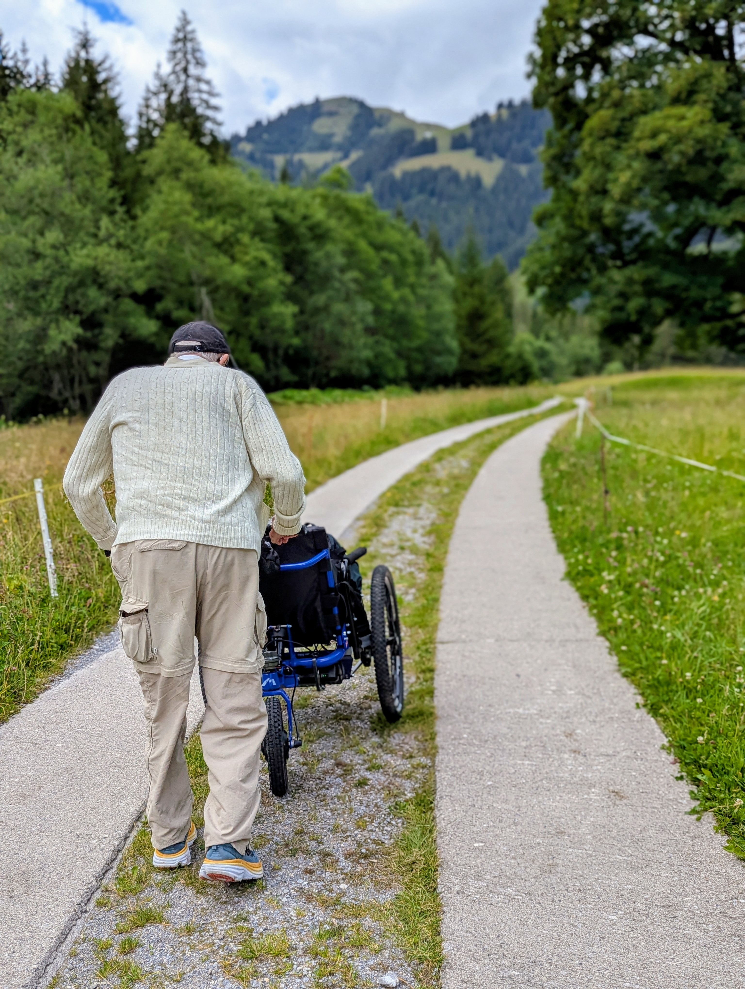 gentleman pushing a wheelchair along a trail path with mountain views
