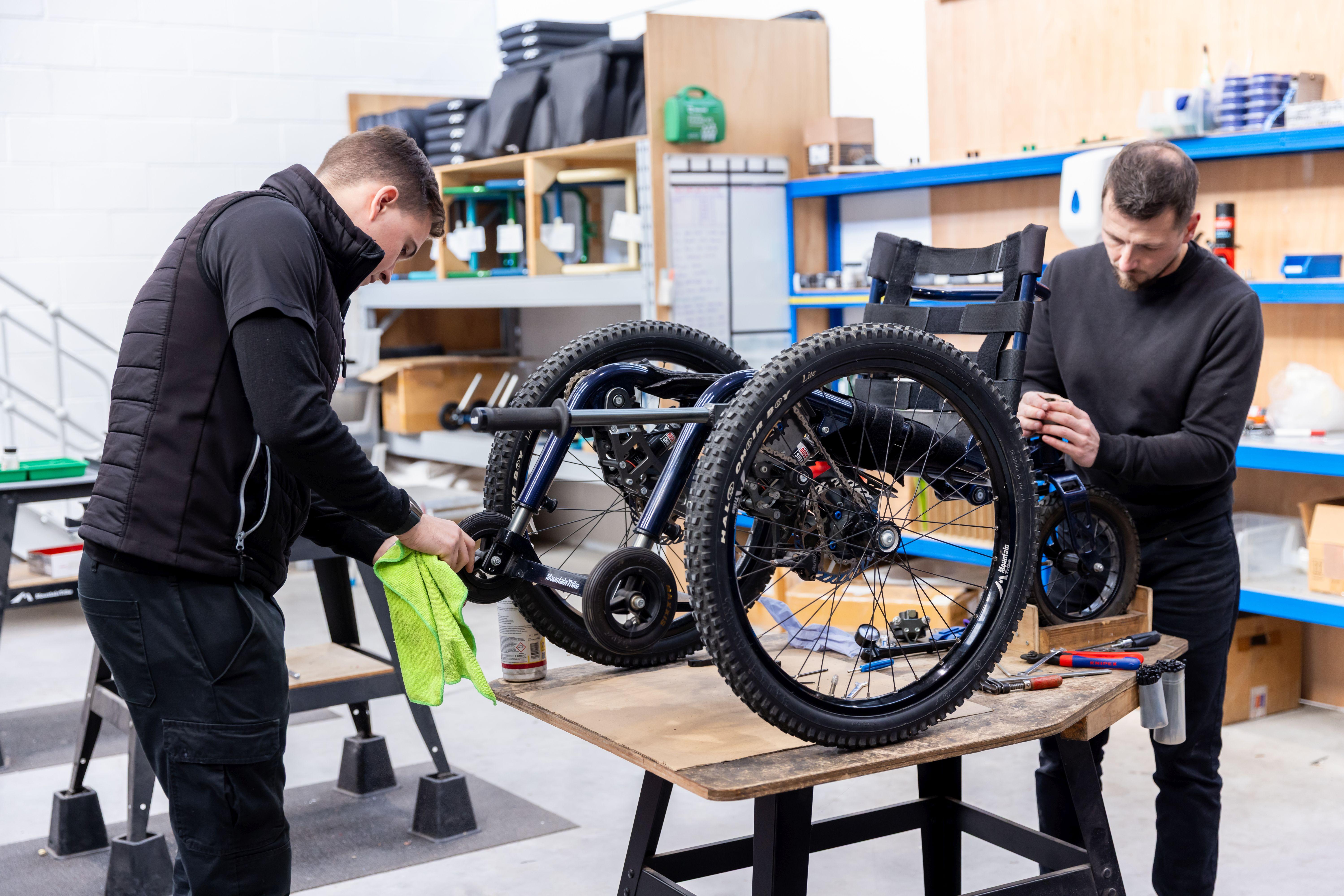 Two men working and servicing the Mountain Trike wheelchair in a workshop