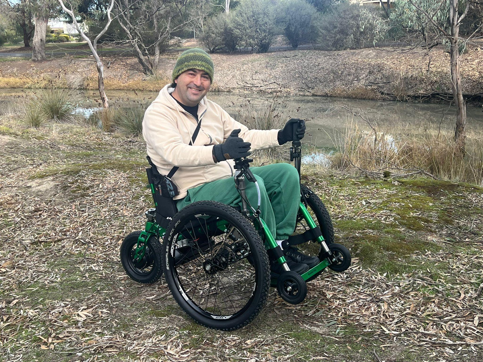 man sat in all terrain wheelchair next to a river